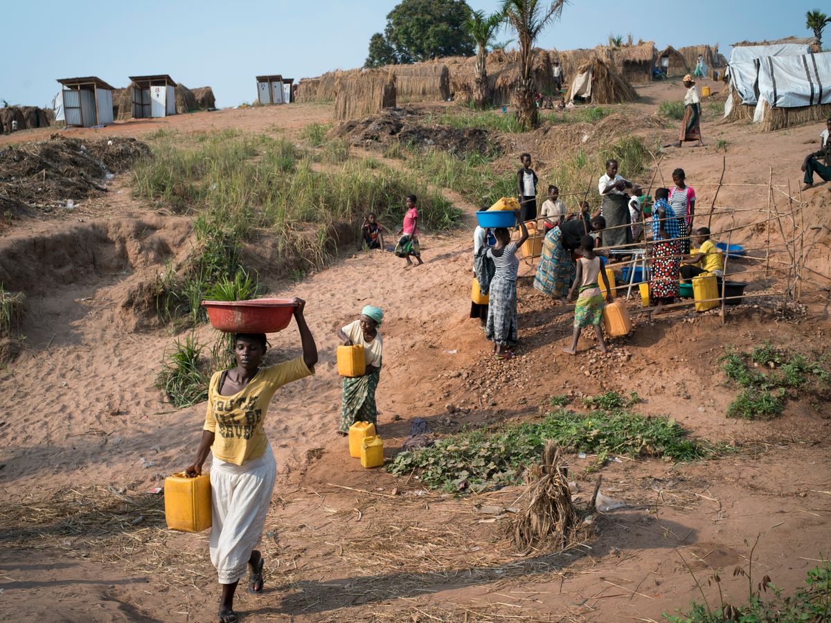 Women and men carrying water in basins and jerrycans up a dusty hillside in Kalemie