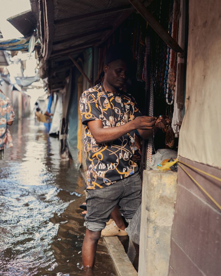 A trader standing in floodwater at his market stall in Lekki, Lagos, still serving