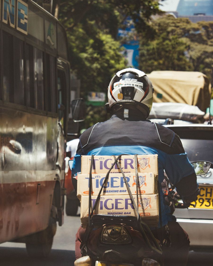 A motorcycle courier in Nairobi carrying stacked boxes through heavy traffic